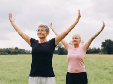 Two women stretching outdoors in a field with arms raised