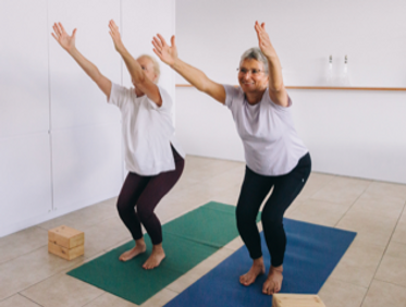 Two women doing a standing stretch together in a studio