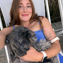 Mobilates member sitting outdoors holding a small grey dog