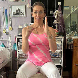 Mobilates member in a pink top sitting cross-legged, smiling and pointing upward
