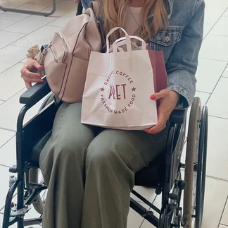 Martha sitting in her wheelchair with a bag on her lap, smiling, wearing a denim jacket and green trousers.