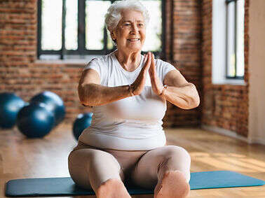 Older woman sitting cross-legged on a yoga mat with hands together, smiling