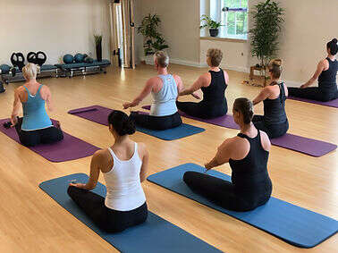 Group taking part in a seated Pilates class, kneeling on mats