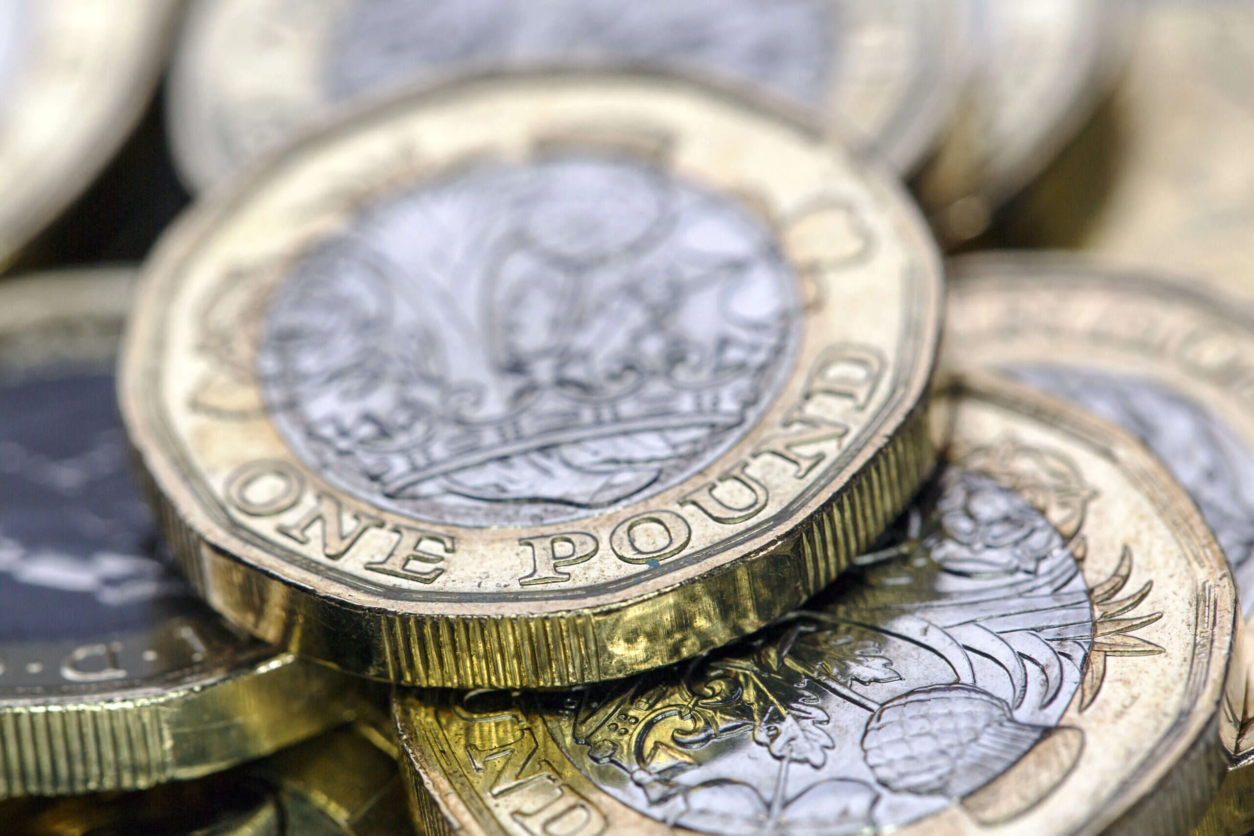 Close-up of stacked British one-pound coins with intricate floral designs and "ONE POUND" text, showcasing metallic textures and details.