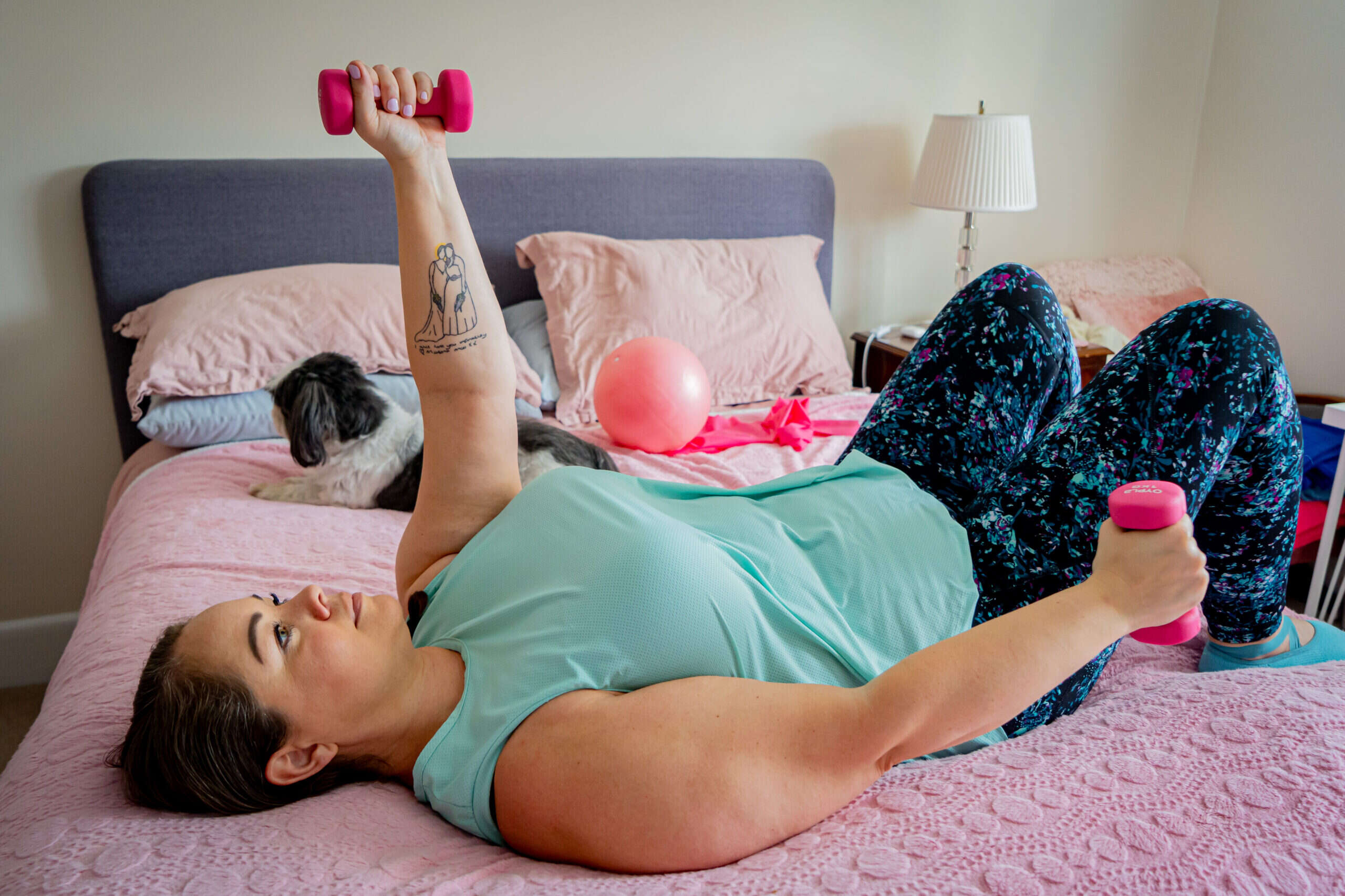Mobilates member exercising with dumbbells from her bed, with her dog beside her