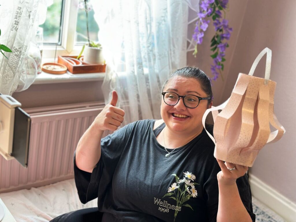 A smiling woman gives a thumbs up while holding a paper lantern she has made.