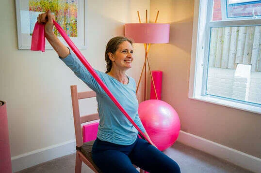 Kerry doing a seated Pilates exercise for an online class and grinning from ear to ear