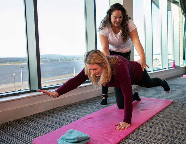 Leanne helping a person get into a pose on their exercise mat