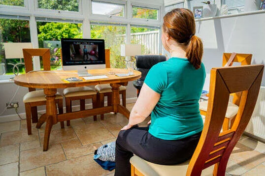 A Mobilates member sitting on a chair for an online class from the comfort of her conservatory