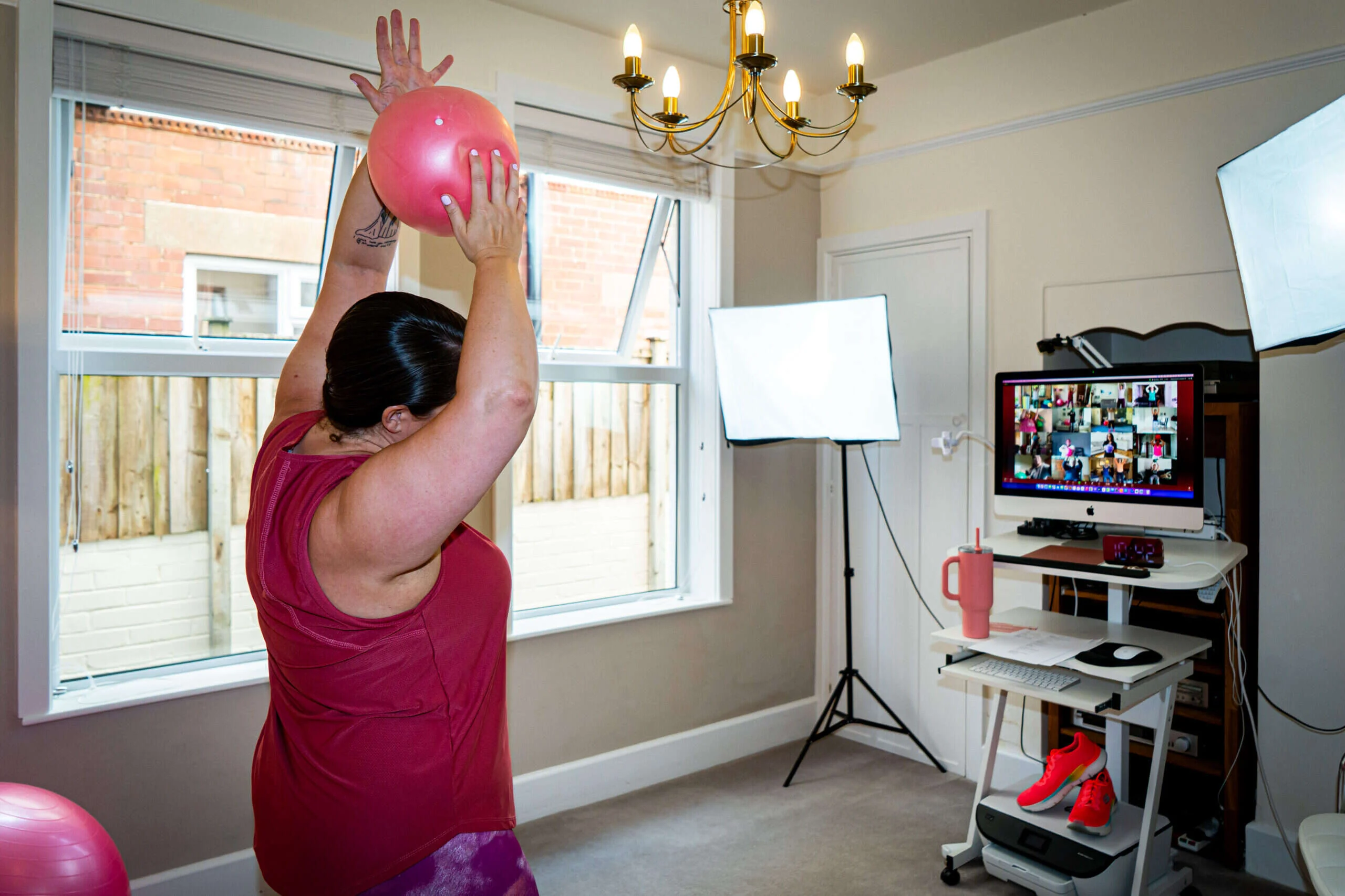 A Mobilates member reaching up with a small pink Pilates ball during an online Mixed Ability class