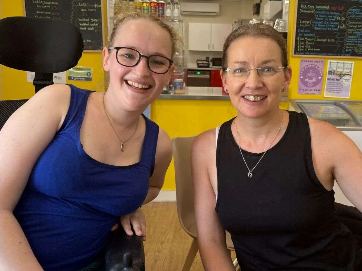 Suzanne sitting with a Mobilates member in a wheelchair at a cafe before her Pilates assessment