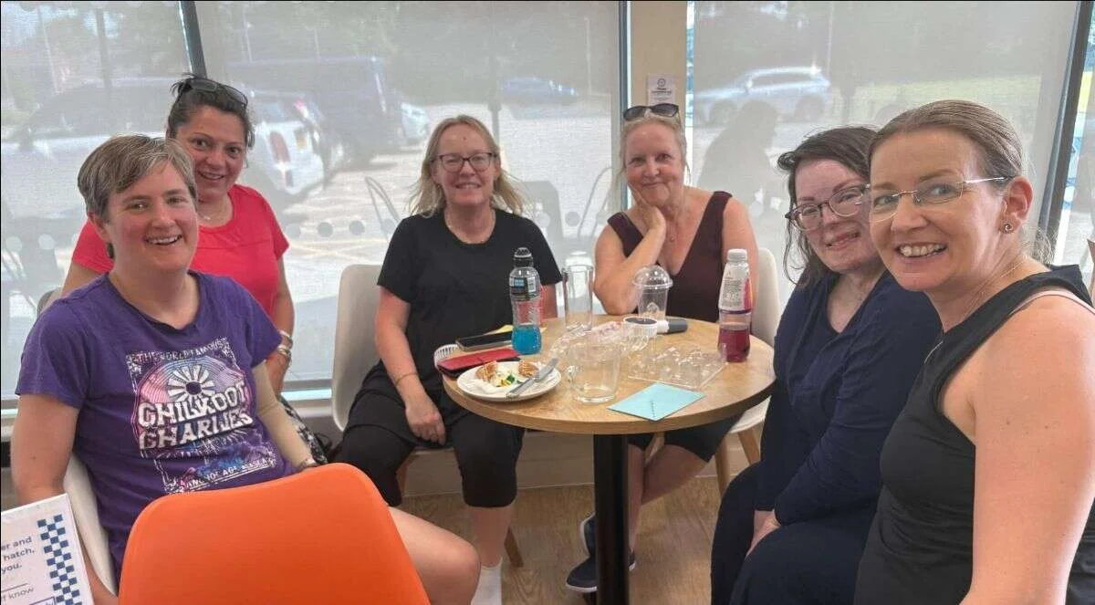 A group of Mobilates members and instructors smiling together around a table after Suzanne's assessment