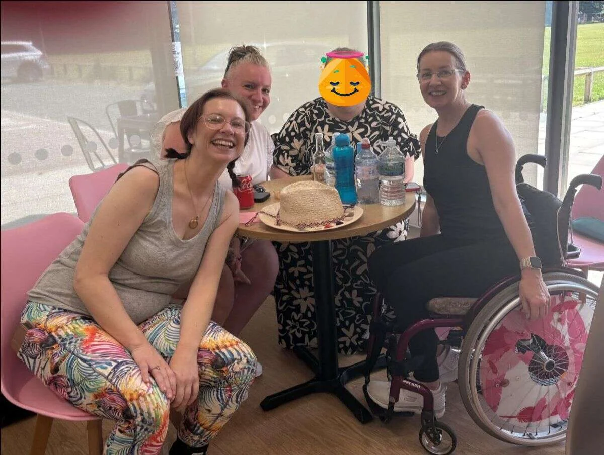 Mobilates members, including one using a wheelchair, gathered around a table celebrating together