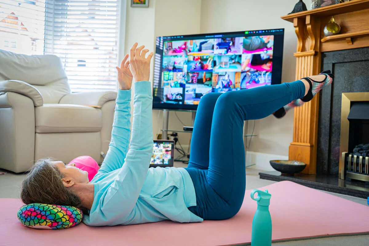 Mobilates member lying on a mat with legs raised and arms stretched overhead during an online Strong & Steady Pilates class