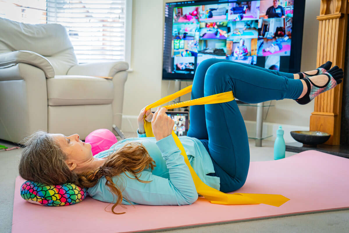 Mobilates member using a resistance band with legs raised during an online Strong & Steady Pilates class