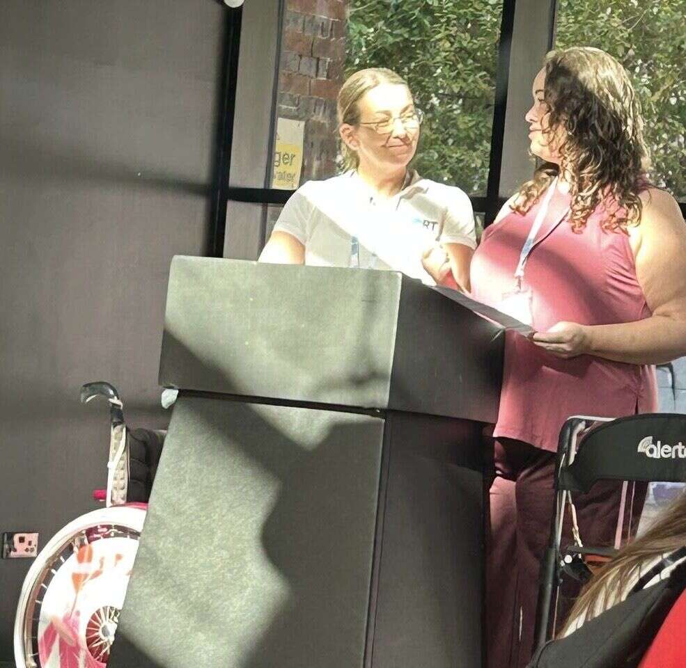 Leanne presenting an award to Suzanne at a lectern at the Include to Improve conference